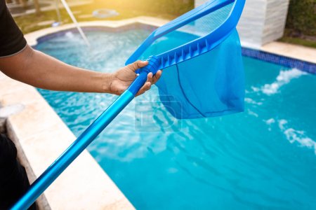 Photo for Person with skimmer cleaning pool, Hands holding a skimmer with blue pool in the background. Man cleaning the pool with the Skimmer, A man cleaning pool with leaf skimmer - Royalty Free Image