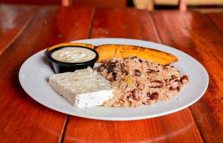 Traditional Gallo Pinto meal with maduro and cheese served. Gallopinto plate with cheese and maduro on wooden table. Nicaraguan food concept