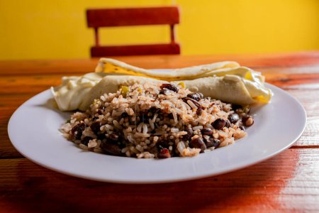 Foto de Gallo pinto con Quesillo servido sobre mesa de madera. Galopinto nicaragüense con quesillo sobre la mesa. alimentos típicos nicaragüenses - Imagen libre de derechos