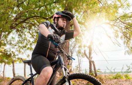Téléchargez les photos : Cycliste potelé épuisé sur son vélo regardant au loin. Cycliste fatigué en vélo sur une route - en image libre de droit