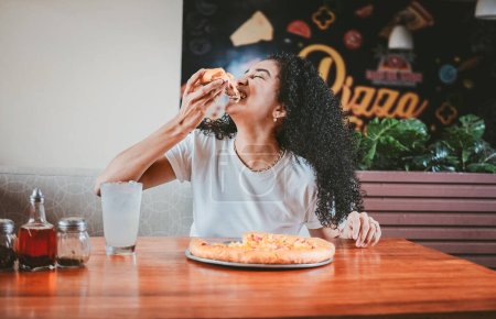 Lebensstil einer afrohaarigen Frau, die in einem Restaurant eine Pizza genießt. Fröhliche Afrohaarfrau isst Pizza in einem Restaurant