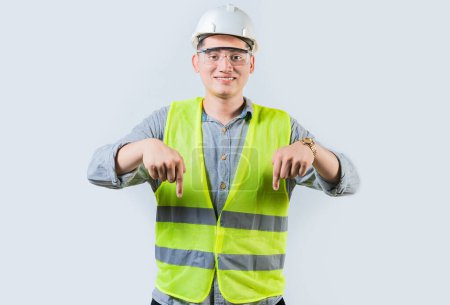 Smiling engineer pointing advertising down isolated. Smiling friendly engineer pointing down isolated