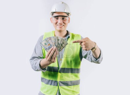 Ingeniero sonriente constructor sosteniendo y apuntando dinero aislado. Ingeniero guapo mostrando y apuntando dinero aislado