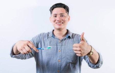 Lächelnder junger Mann mit Zahnbürste gestikuliert. Person hält Zahnbürste mit erhobenem Daumen. Kerl mit Zahnbürste und OK-Geste