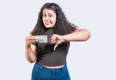 Unzufriedene junge Frau hält vereinzelt einen Dollarschein mit gedrücktem Daumen in der Hand. Trauriges Mädchen hält einen 100-Dollar-Schein mit gesenktem Daumen