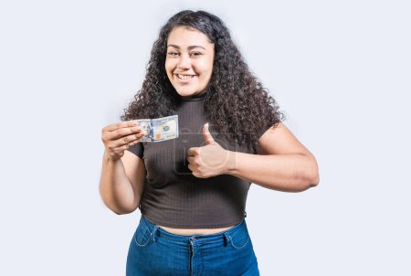 Smiling girl holding a 100 dollar bill gesturing approved. Young woman holding a 100 dollar bill with thumb up