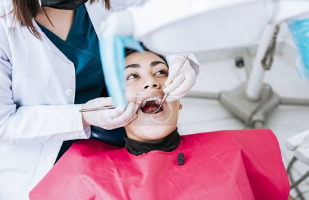 Draufsicht des Zahnarztes, der Patientin im Liegen reinigt. Zahnärztin untersucht Mund zu Patient im Liegen, Zahnärztin untersucht Mund zu Patient im Liegen