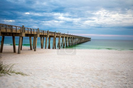 Pensacola Beach Fishing Pier extending out into the Gulf of Mexico during a pastel colored sunset sunset on a cloudy evening. 