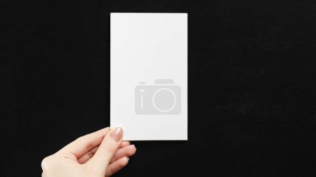 Photo for Blank card. Information letter. Stationery note. Female hand showing white mockup paper sheet with empty space on black background. - Royalty Free Image