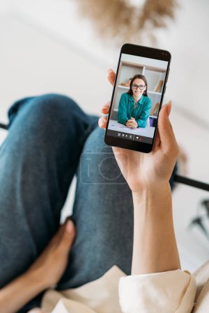 Photo for Video call. Online counseling. Mobile conference. Relaxed woman watching cheerful smart female expert on phone screen at home interior. - Royalty Free Image