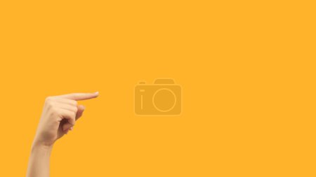 Photo for Recommending gesture. Right direction. Female hand finger pointing demonstrating blank area on orange empty space commercial background. - Royalty Free Image