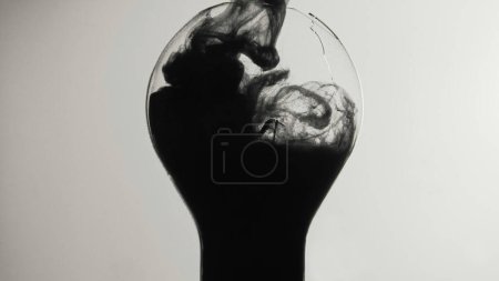 Photo for Black smoke. Broken light bulb. Ink water shot. Dark energy. Toxic fume cloud filling cracked glass lamp on white abstract copy space background. - Royalty Free Image