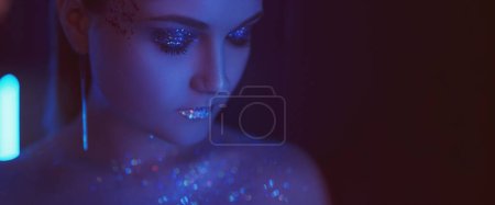 Photo for Neon beauty. Glitter makeup. Nightclub vogue. Portrait of purple blue color light woman with sparkling face skin eyeshadow lips on dark copy space background. - Royalty Free Image