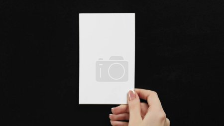 Photo for White card. Empty note. Invitation letter. Female hand showing clean mockup paper sheet with copy space on black commercial background. - Royalty Free Image