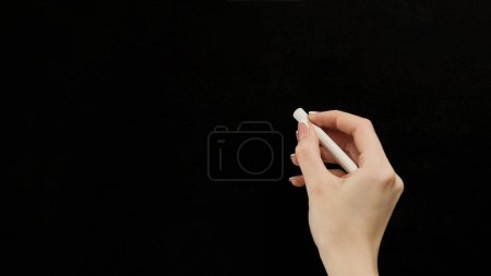 Chalk writing. Back to school. Learning education. Female teacher hand at blank clean blackboard with copy space on black information background.