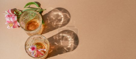 Photo for Alcohol drink. Vacation beverage. Exotic booze. Couple of brown rum glasses with flower decoration on beige empty space background. - Royalty Free Image