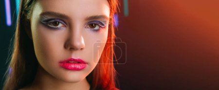 Photo for 90s face. Retro makeup. 2000s fashion. Red color neon light closeup portrait of teen girl model with purple eyeshadow pink lips artistic look on dark copy space background. - Royalty Free Image