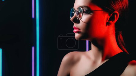 Téléchargez les photos : 90s look. Optic fashion. Retro eyewear. Red purple blue color neon light profile portrait of teen girl model face in glasses on dark black empty space background. - en image libre de droit