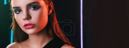Photo for 90s look. Fashion makeup. Retro 2000s beauty. Neon light closeup portrait of confident teen girl model face with artistic visage on black copy space background. - Royalty Free Image