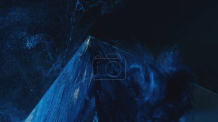 Téléchargez les photos : Paint splash. Smoke pyramid. Ink water. Ice hill. Defocused blue color steam floating over frozen glass cube angle edge on dark abstract background. - en image libre de droit
