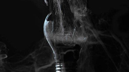 Foto de Lamp explosion smoke cloud. Power failure. Defocused gray color vapor haze in broken glass light bulb on dark black night abstract background. - Imagen libre de derechos
