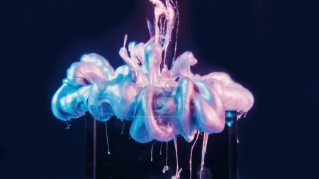Téléchargez les photos : Ink drop. Neon fluid. Paint water. Fantasy cloud. Pink blue iridescent color glowing liquid splash on glass cube dark abstract background. - en image libre de droit