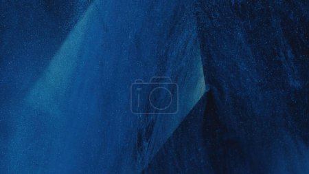 Téléchargez les photos : Dust mist. Glitter texture. Paint drip. Defocused blue color sparkling fluid ink smoke over cube angle in water on dark abstract background. - en image libre de droit