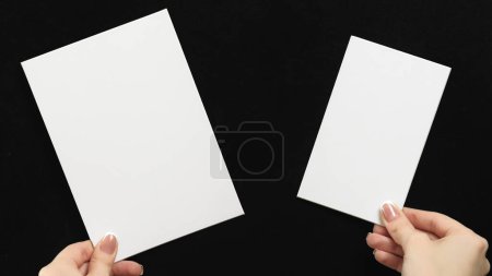 Photo for Mockup notes. Presentation card. Information letter. Female hands holding two white clean blank paper sheets with copy space on black advertising background. - Royalty Free Image