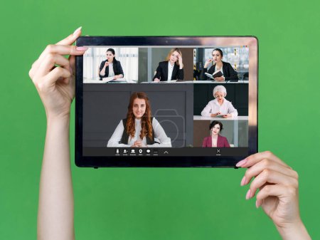 Foto de Video chat. Business meeting. Corporate telework. Professional female team discussing work online on tablet screen in hands on green. - Imagen libre de derechos