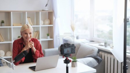 Photo for Content creator vlog stream. Social media communication. Senior influencer woman speaking recording video on camera on tripod on defocused light home interior with free space. - Royalty Free Image