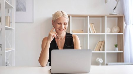 Photo for Video conference. Web chat. Online communication. Cheerful smiling mature business woman using laptop working at light modern home office interior with free space. - Royalty Free Image