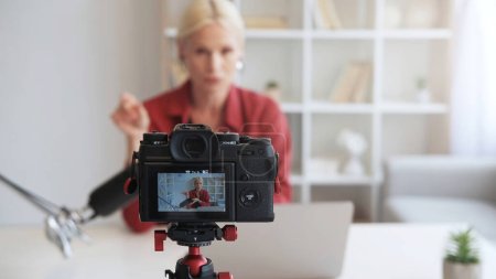 Photo for Influencer vlog. Live streaming. Online coaching. Mature blogger woman talking recording video interview on camera on tripod on defocused interior with free space. - Royalty Free Image