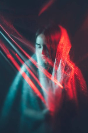 Pure soul. Female tenderness. Defocused peaceful woman face silhouette wearing bubble wrap in blur red blue color light rays on dark.