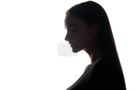 Female loneliness. Solitude contemplation. Dark backlit profile silhouette of sad unhappy pensive woman face on white empty space background.