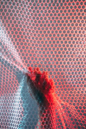 Photo for Freedom trap. Emotional struggle. Defocused red blue color light female hand grasping transparent polyethylene bubble wrap textured wall conceptual background with copy space. - Royalty Free Image