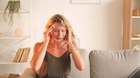 Photo for Exhausted day. Suffering woman. Headache frustration. Feeling bad sick lady holding neck massaging head temples sitting sofa light room interior. - Royalty Free Image
