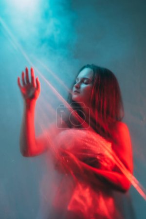 Foto de Iluminación espiritual. Sanación del alma. Silueta de mujer inspirada relajada desenfocada en rayos de luz de color azul rojo cielo cielo humo nube. - Imagen libre de derechos