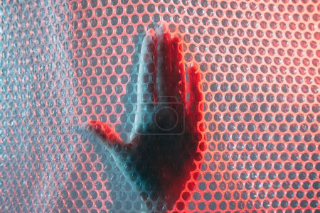 Photo for Stop gesture. Plastic pollution. Environment protection. Red blue color light female hand warning signal behind bubble wrap texture polyethylene background. - Royalty Free Image