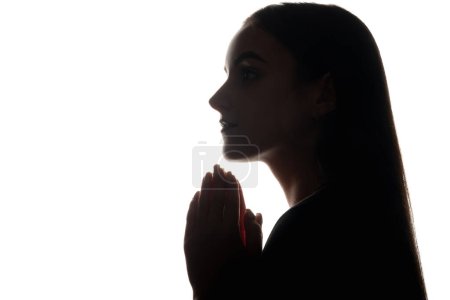 Photo for Prayer silhouette. Christian faith. Hope forgiveness. Dark backlit profile portrait of religious woman with folded hands on white empty space background. - Royalty Free Image