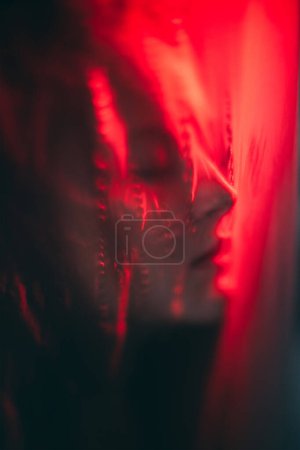 Photo for Nightmare dream. Dark consciousness. Red color light defocused tranquil woman face silhouette sleeping with closed eyes covered with distressed polyethylene plastic film. - Royalty Free Image