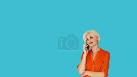 Foto de Comunicación móvil. Mujer escéptica. Conexión virtual. Mujer infeliz de mediana edad hablando teléfono inteligente posando espacio de copia azul. - Imagen libre de derechos