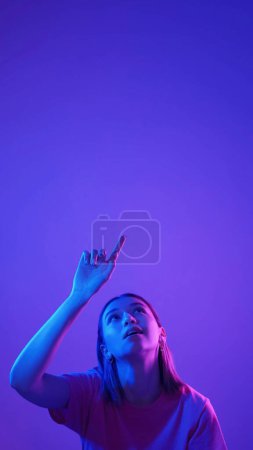 Photo for Virtual touch. High tech click. Neon color light girl pressing invisible futuristic button selecting option isolated on blue pink empty space background. - Royalty Free Image
