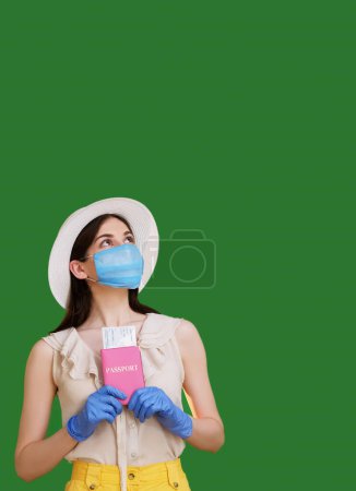 Photo for Pandemic tourism. Passport control. Dreaming woman in protective mask gloves holding passport and tickets waiting departure to resort isolated green empty space background. - Royalty Free Image