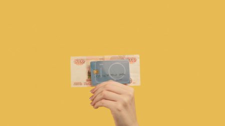 Téléchargez les photos : Prêt d'argent. Transaction bancaire. Femme main tenant des roubles 5000 et carte de crédit sur fond jaune. - en image libre de droit