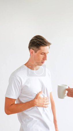 Photo for Food poisoning. Strong stomachache. Medical problems. Sick unhealthy man touching painful stomach hand giving cup with medicine isolated on white empty space background. - Royalty Free Image