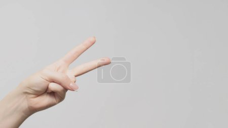 Foto de Un gesto de mano. Señal de victoria. Mujer mostrando dos dedos apuntando espacio de copia sobre fondo gris claro. - Imagen libre de derechos