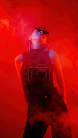 Photo for Color light portrait. Dancing woman. Satisfied girl in black sunglasses relaxing enjoying night life on red neon smoke background. - Royalty Free Image