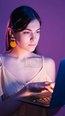 Photo for Night online job. Network surfing. Concentrated focused neon color light girl typing laptop working online communication isolated on purple background. - Royalty Free Image