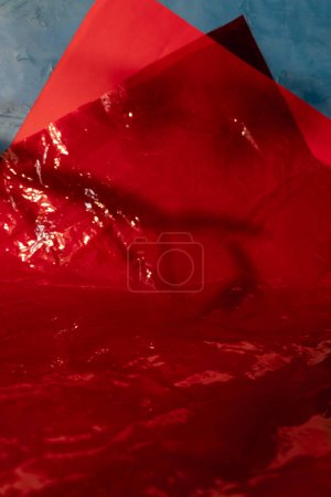 Photo for Creased film abstract background. Crumpled layers. Shiny red color wrinkled paper sheet on blue surface geometric design showcase with free space. - Royalty Free Image