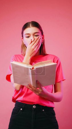 Photo for Surprising reading. Shocked literature. Astonished excited girl holding book covering mouth scared with storyline novel isolated on neon color pink background. - Royalty Free Image